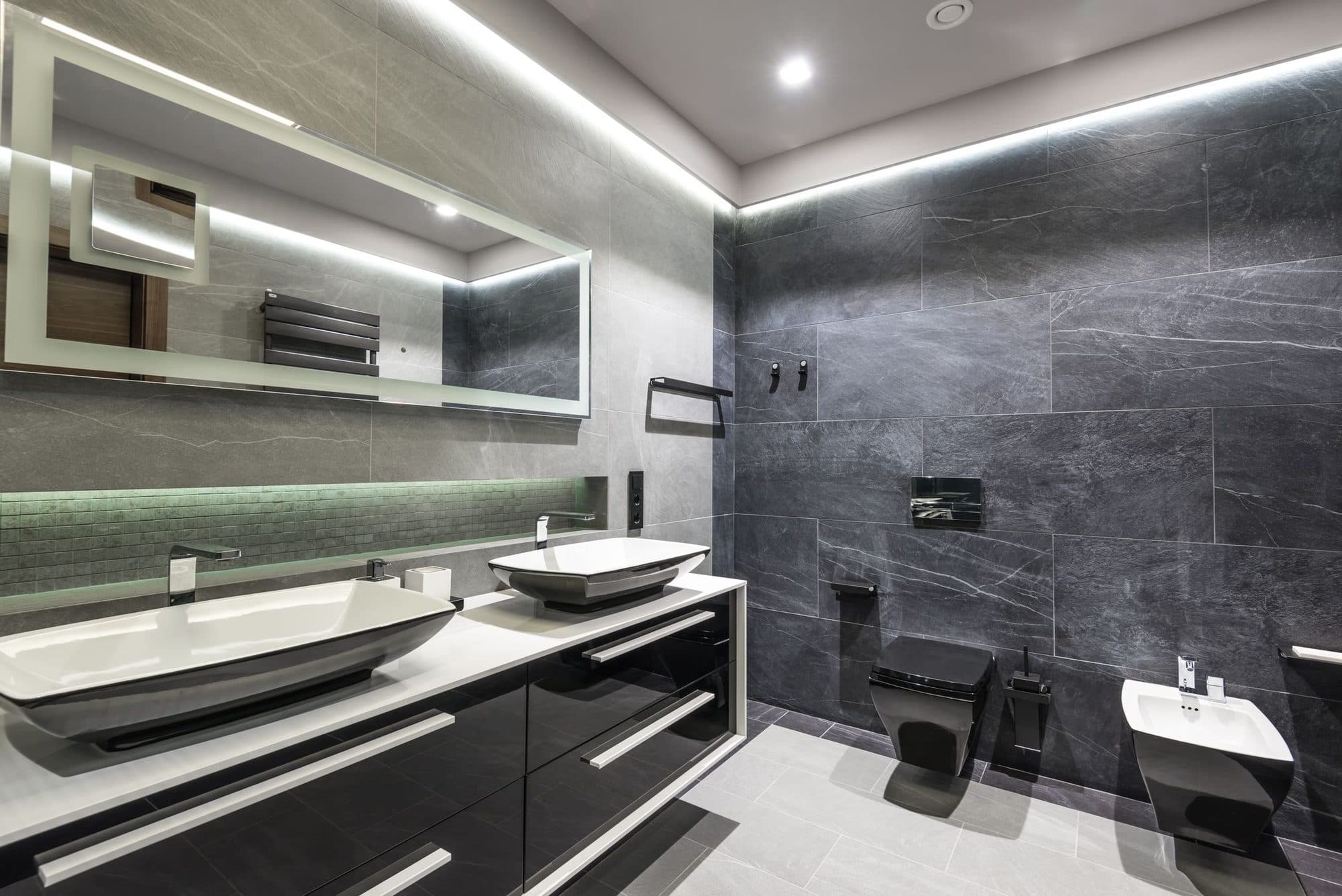 A bathroom with twin basins and dark tiled walls