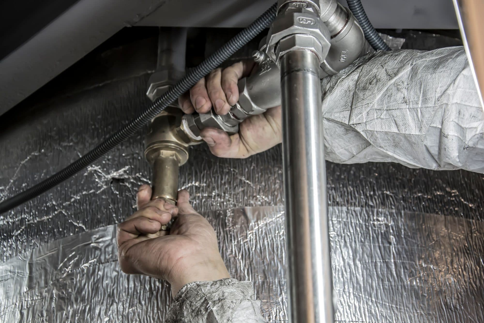Hands fitting a supply connection beneath a kitchen sink