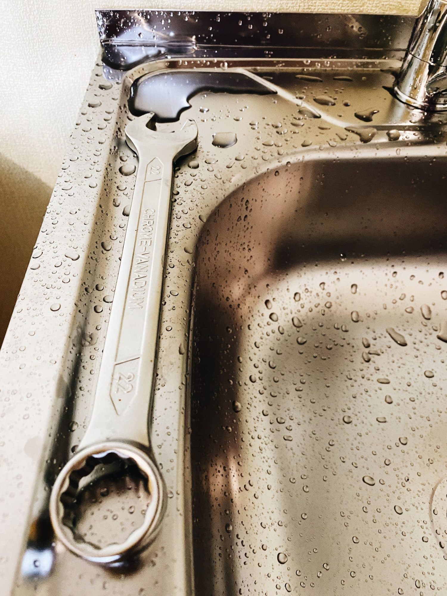 A spanner resting in a wet stainless steel sink